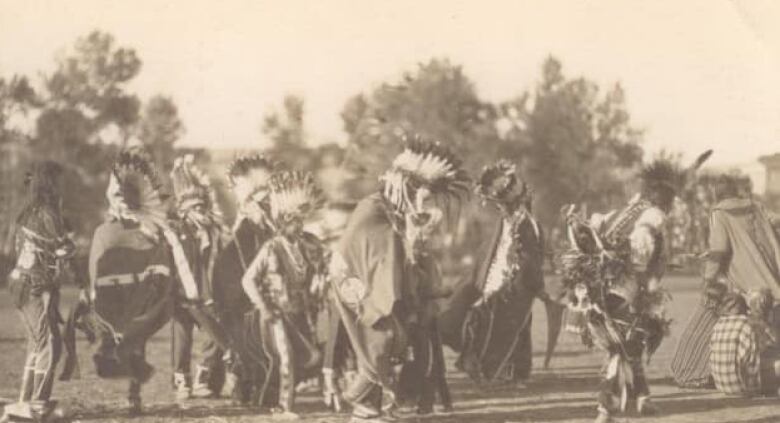 Black and white photo of a group of First Nations can be seen together dressed in traditional clothing. Written on the photo are the words war dance.