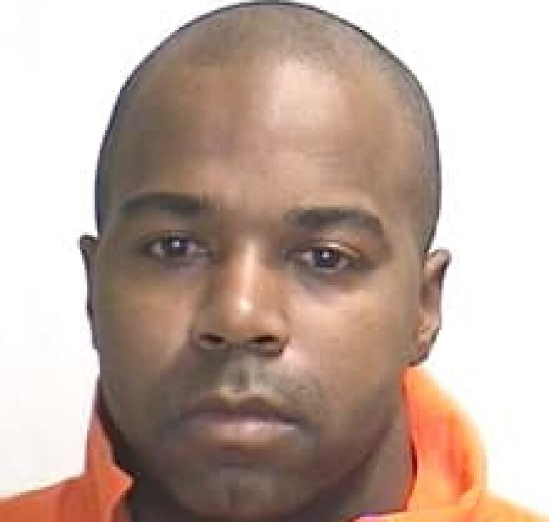 A close-up of a Black man wearing a prison-issued orange jumpsuit.