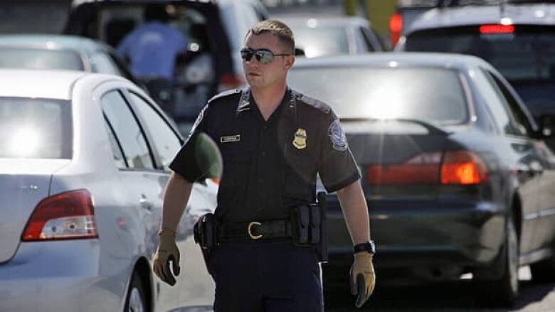 A U.S. Customs and Border Protection officer walks through a line of cars