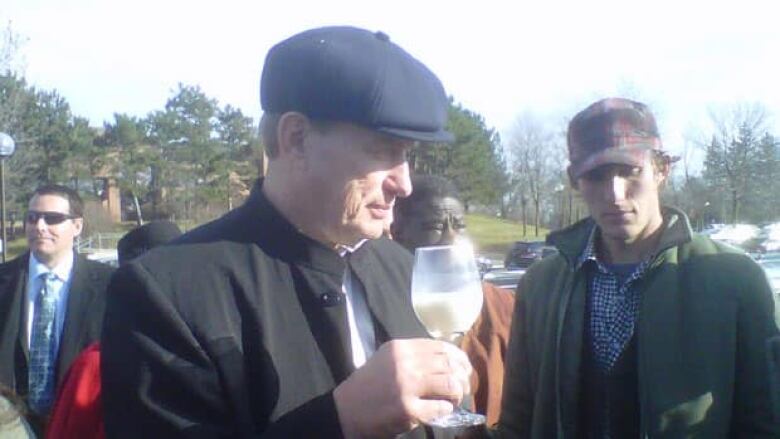 A man in a hat holds a glass of milk. 