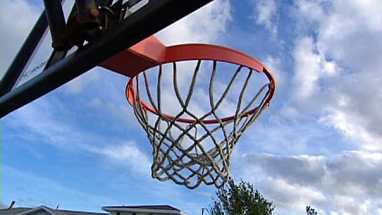 An orange basketball rim is pictured under a cloudy blue sky.