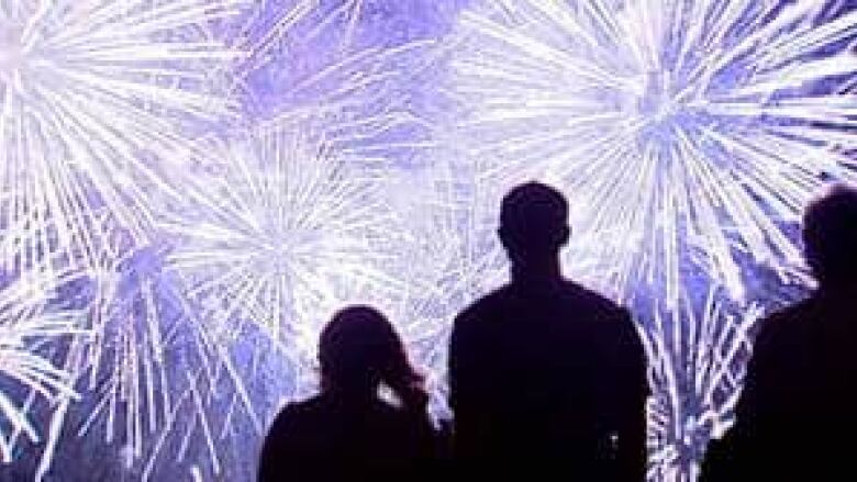 Dozens of fireworks light up the sky, with people seen watching them in silhouette.