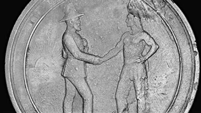 A coin shows two men shaking hands, one dressed in traditional First Nations clothing, the other in formal British official clothes.