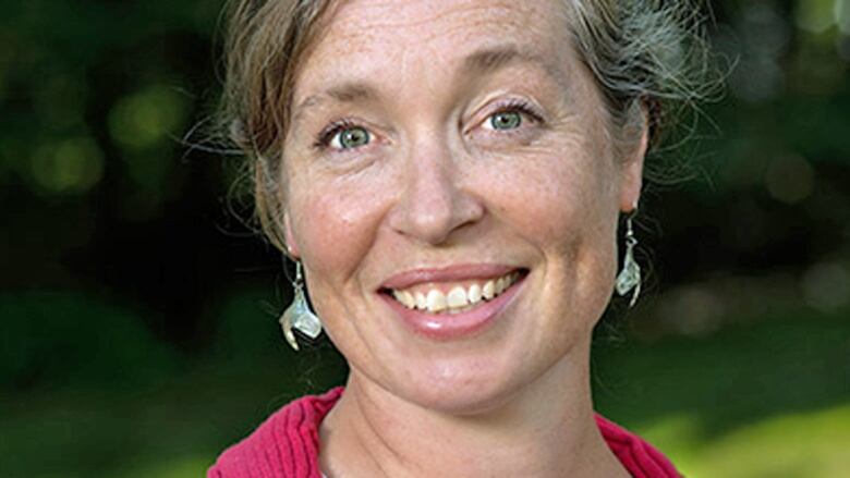 A woman with grey hair in an updo smiles at the camera. She is wearing dangly earrings. 