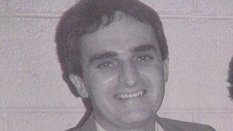 A smiling man with dark hair looks into the camera in a black and white photo