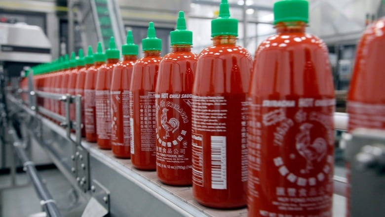 A line of clear bottles with red sauce in them capped with a green spout