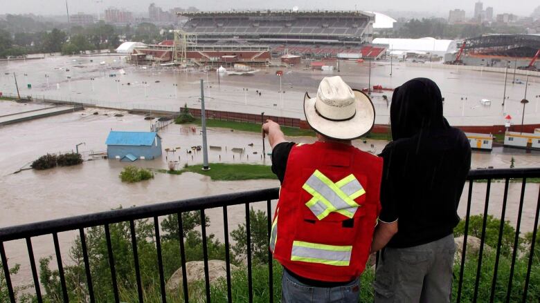 Two people, one in cowboy hat, look out over a flooded Stampede grounds.