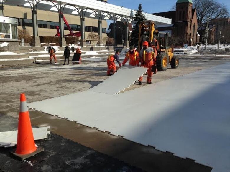 Workers installing synthetic ice at an outdoor square.