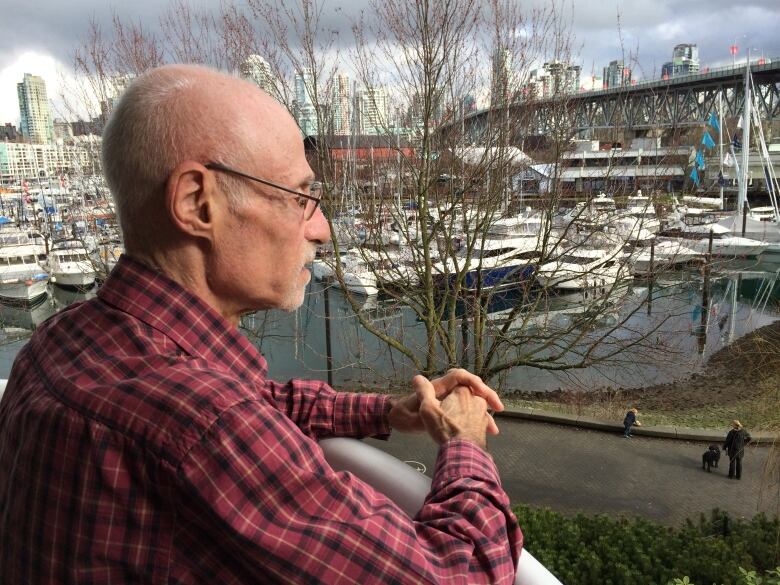 A man looks from his balcony, across a harbour filled with boats.