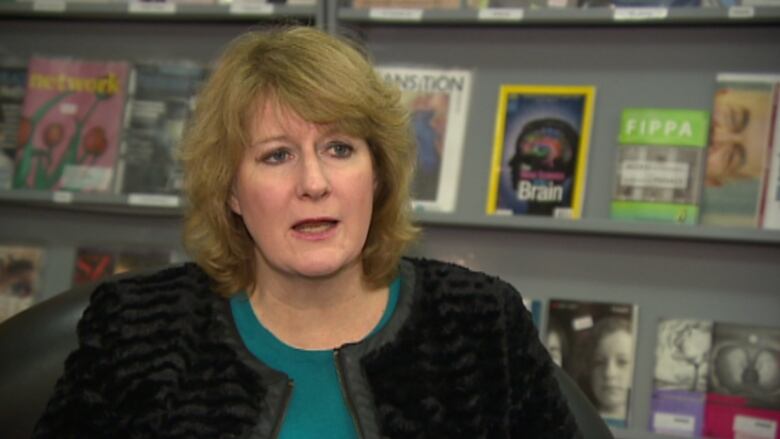 A woman sits in front of a book shelf.