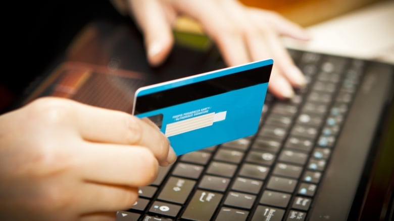 A person holds a credit card while typing with their other hand.