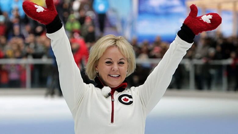 A woman with short blonde hair is seen smiling. She is wearing red gloves and a white top.