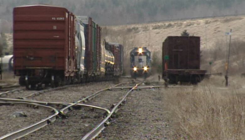 A train engine with its lights on is on train tracks with several rail cars on sidings next to it.