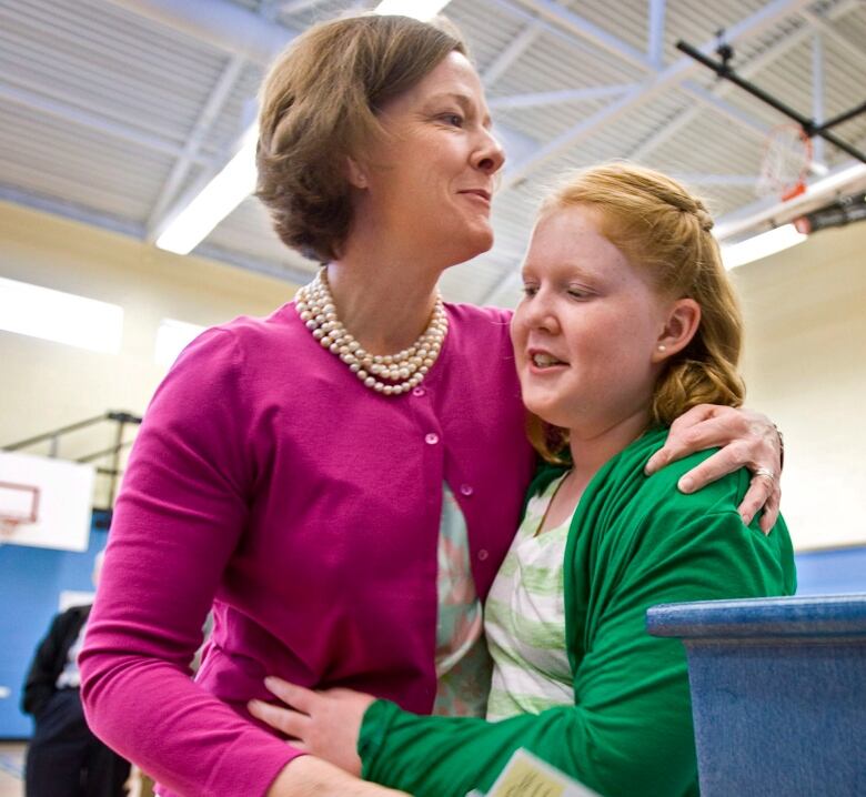 A woman hugs a girl in a basketball court. 