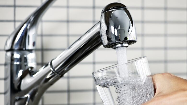 Person filling glass of water at tap.