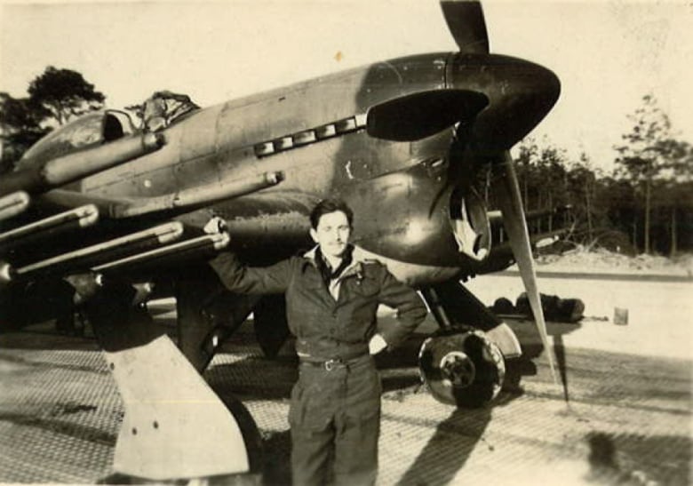 Vintage photo pf a soldier in uniform standing in front of a Typhoon airplane.