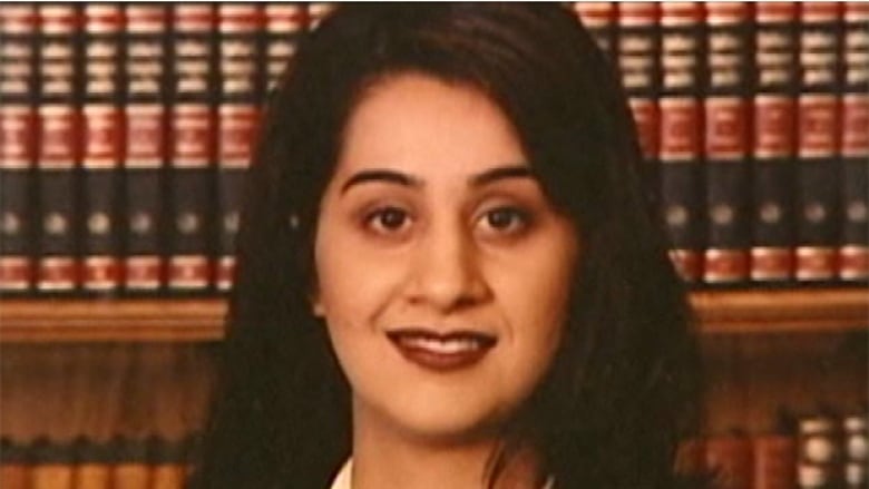 An Indian woman smiles in front of a bookcase.