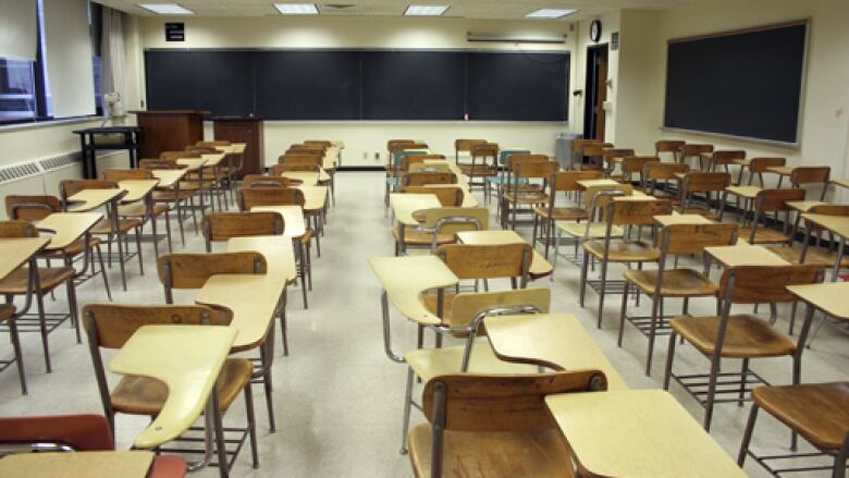 Rows of empty desks face a blank chalk board.