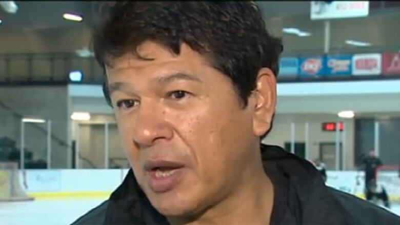 A closeup of hockey coach Ted Nolan, only his face shown, at a hockey rink. He has dark hair cut short.