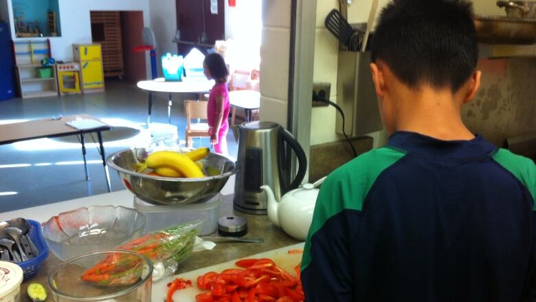 A teen with his back to the camera prepares food in a small kitchenette in a school. 