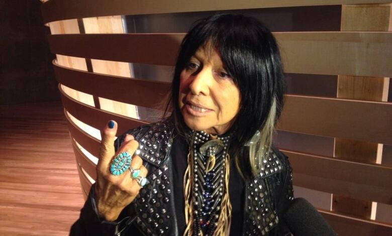 A woman in a leather jacket speaks to reporters in a darkened room.