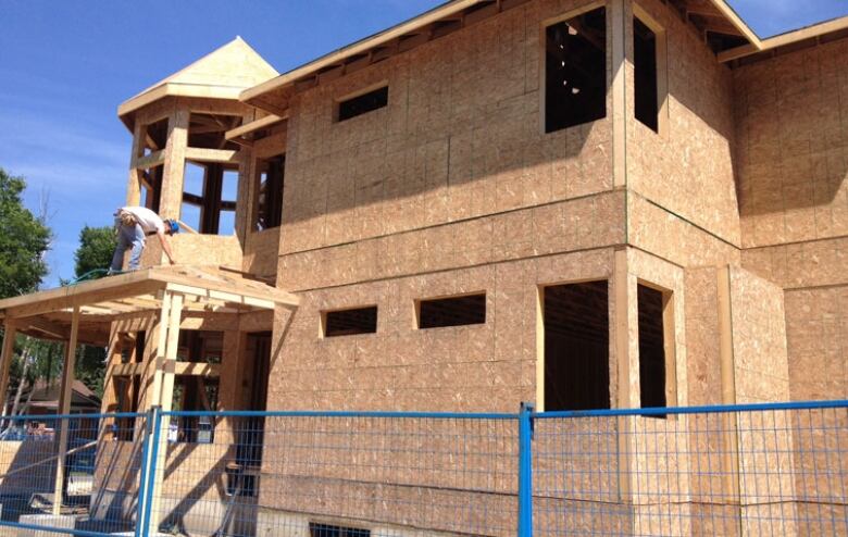 a person works on a higher level of a house under construction that's mostly just wood with a blue safety fence in front