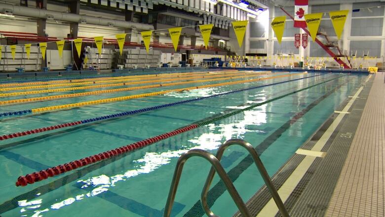 The water inside an indoor swimming pool is calm. The pool, divided into lanes, is empty.