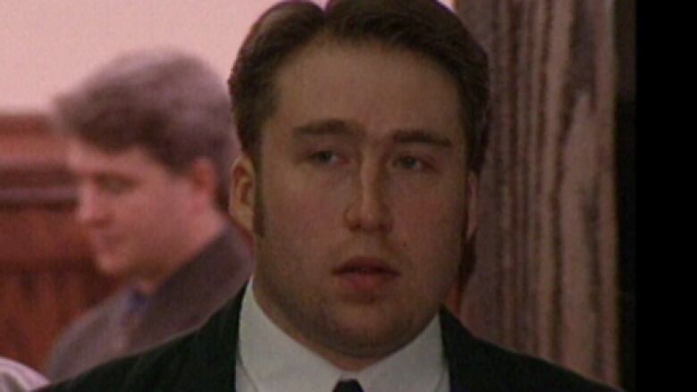 A man with long sideburns who is wearing a suit and tie walks through a courthouse.