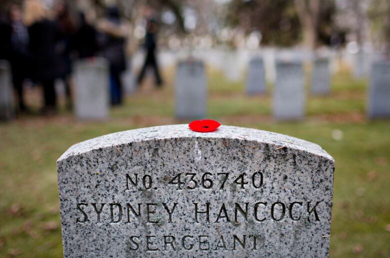 A bright red poppy sits atop a grey headstone inscribed with the words, Sergeant Sydney Hancock, 