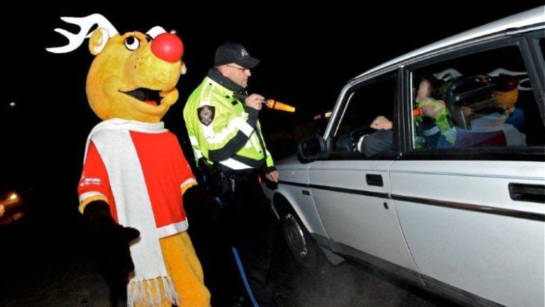 A man in Reindeer body suit stands aside a police official in uniform beside a white car.  