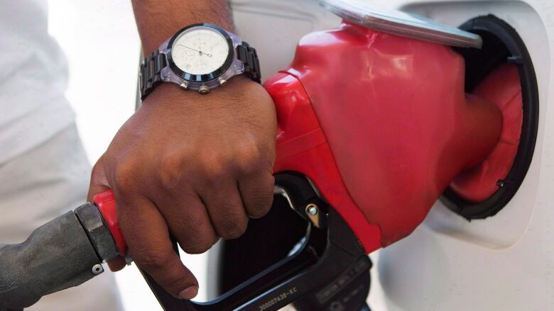 A hand rests on a gas pump while it fills a car with gasoline.