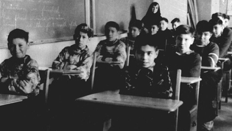 Black and white photo of boys sitting at wooden desks in school 