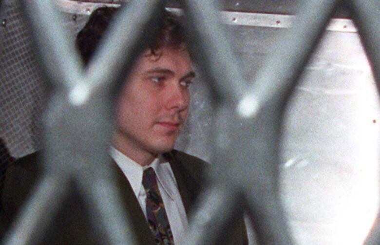 A man in a tie sits in a prison van.