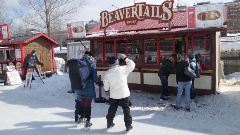 Two skaters gaze at the menu of a food stand on a frozen waterway.