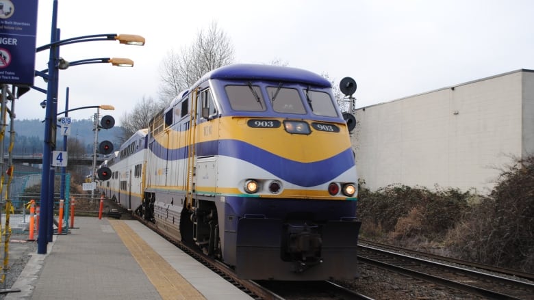 A white, blue and yellow stripped train heading to a station platform outside. 