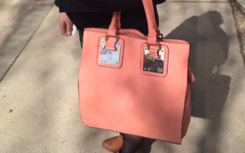 A pink handbag is seen hanging from a person's forearm.  