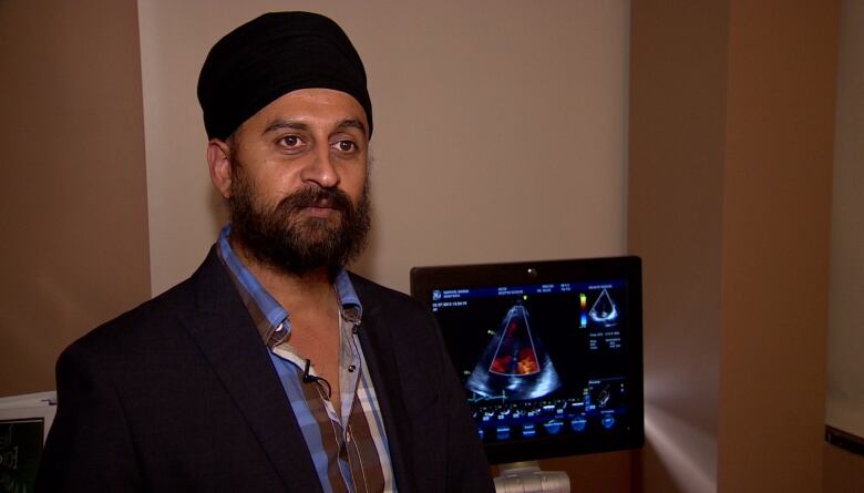 Dr. Anmol Kapoor, wearing a black blazer and turban, is standing in front of a screen showing a medical scan.