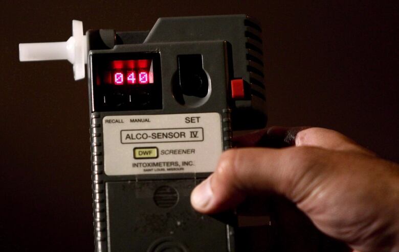 A close up  of a hand holding a breathalyzer machine. 