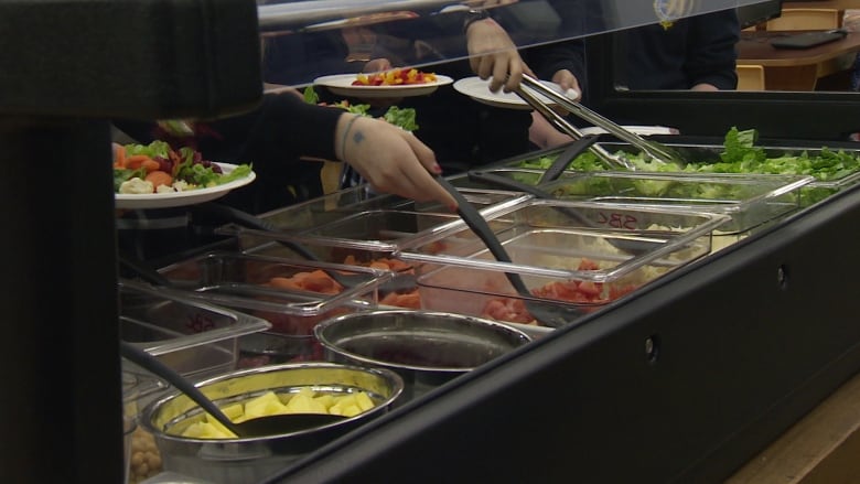 Young people serve themselves at a salad bar.