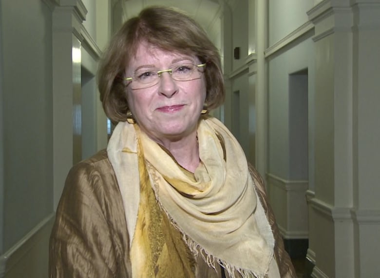 A woman wearing a gold-coloured dress speaks in a corridor.