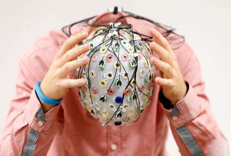 A person poses with an electroencephalography cap, which has a lot of wires .