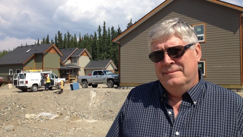 A man with white hair and glasses stands in front of some newly finished houses.