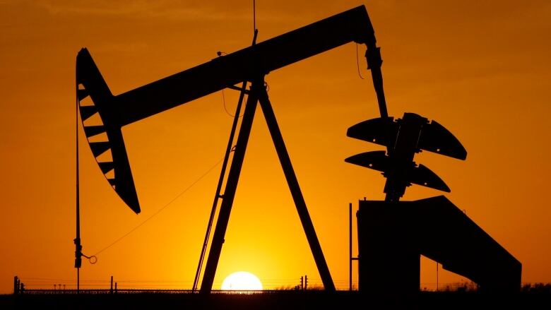 A photo of a pump jack in silhouette against the sun.