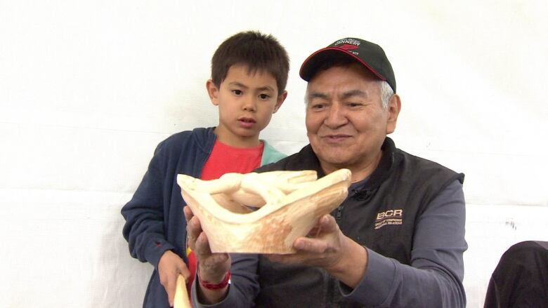 An old man in cap shows a bowl to a young child.