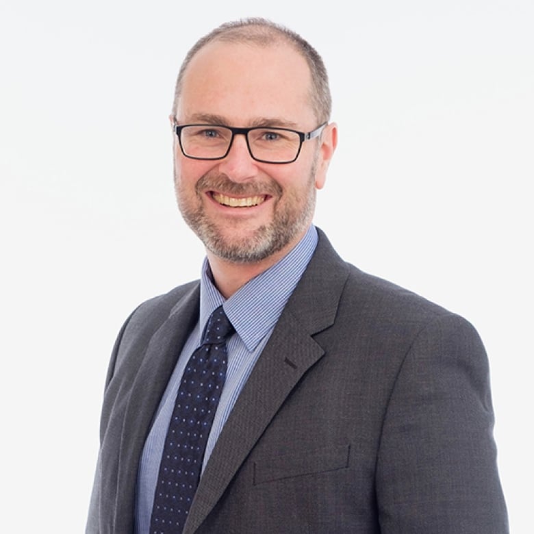 Man wearing a jacket and tie on a white background smiles to camera.