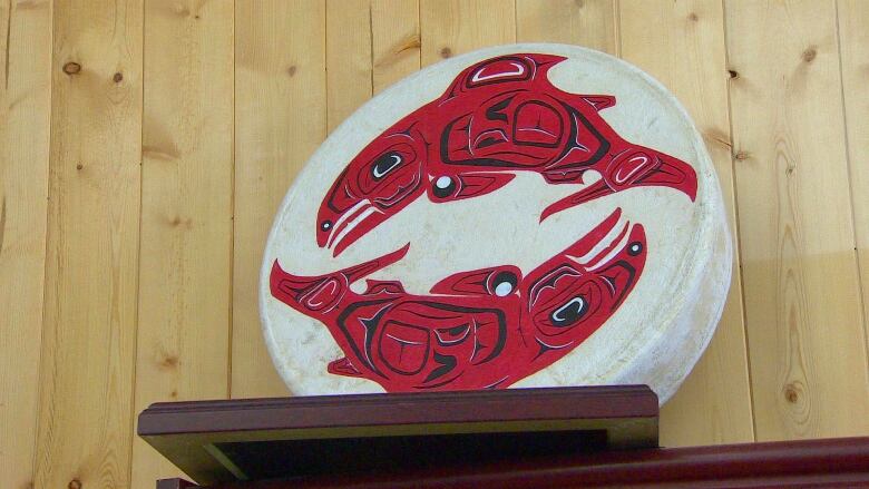 An Indigenous drum, painted with depictions of chinook salmon, stands on a shelf.