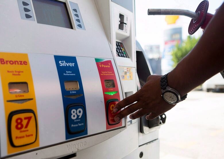 A hand presses a button at a gas pump.