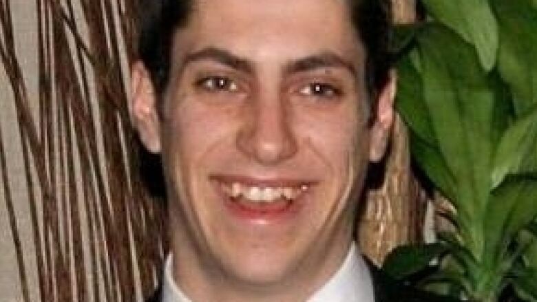 A young man with short brown hair wears a suit and tie.