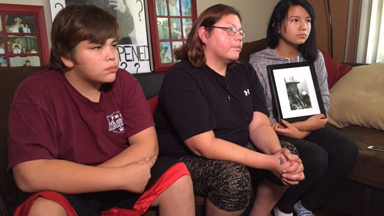 Woman and two teens hold a black and white photo of a boy.