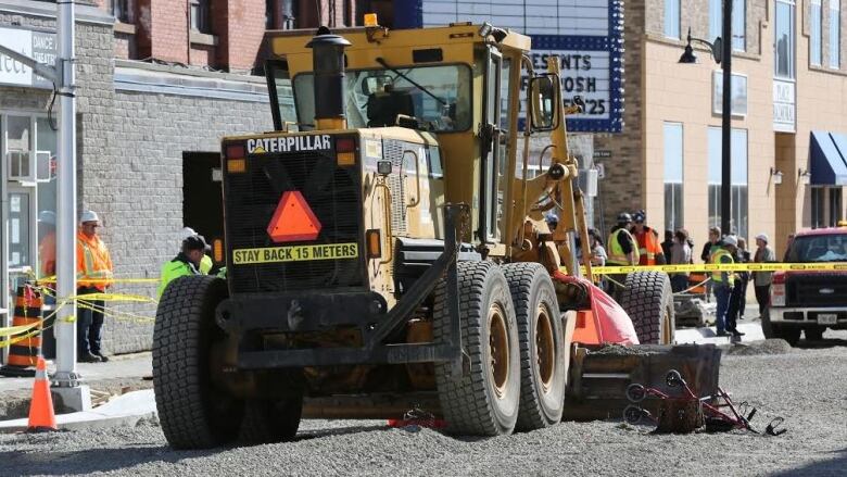 A walker sits next to a grader on a downtown street covered in gravel, with police tape strung around it. 